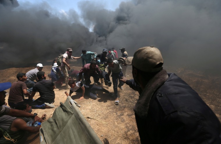 Image: A wounded Palestinian demonstrator is evacuated as others take cover from Israeli fire and tear gas