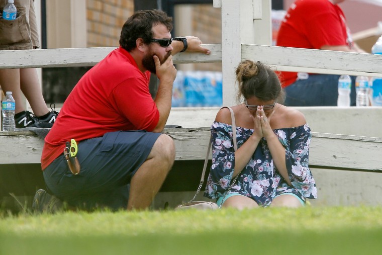 A woman prays in the grass while parents wait to reunite with their kids.