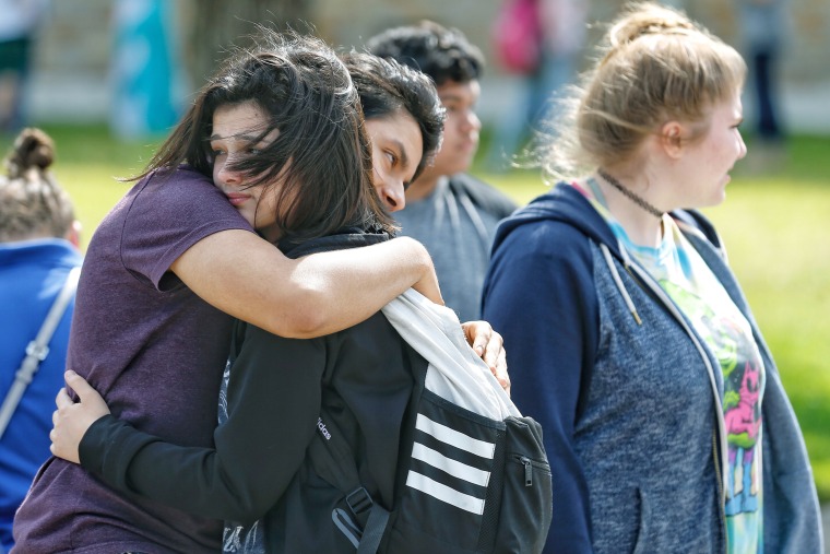 Freshman Caitlyn Girouard, center, hugs her friend outside the Alamo Gym, where students and parents wait to reunite following the shooting.