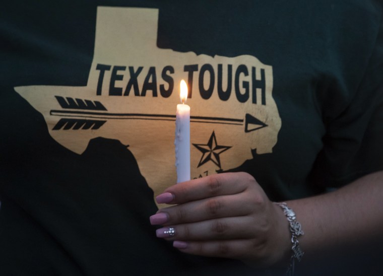 Image: A woman in Texas t-shirt holds a candle during a vigil