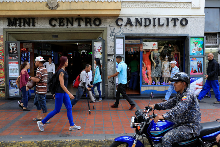 Image: People walk past stores in downtown Caracas