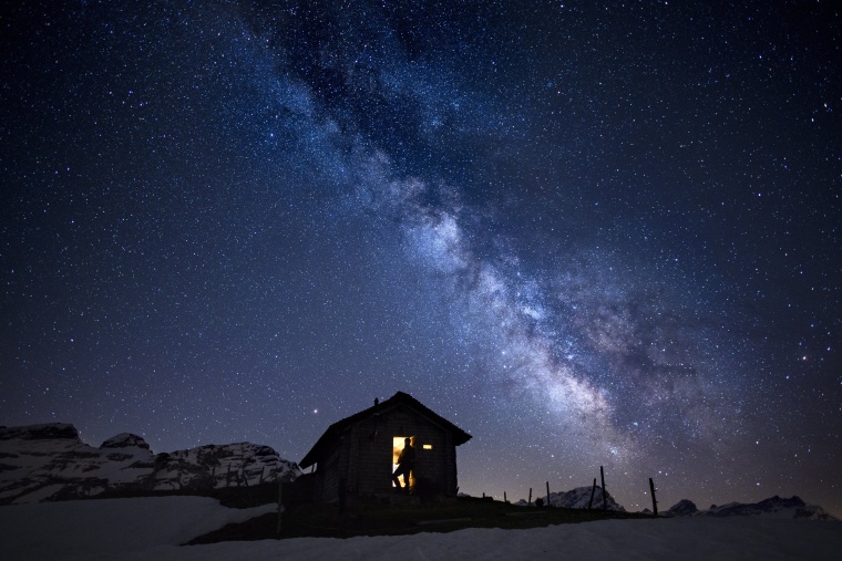 Image: A man stands inside cabin with a view of the Milky Way