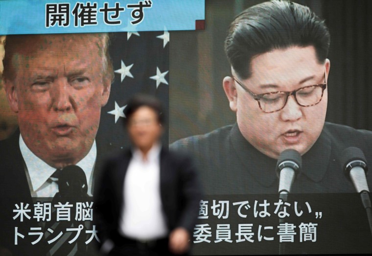 Image: A pedestrian walks in front of a screen in Tokyo showing Donald Trump and Kim Jong Un