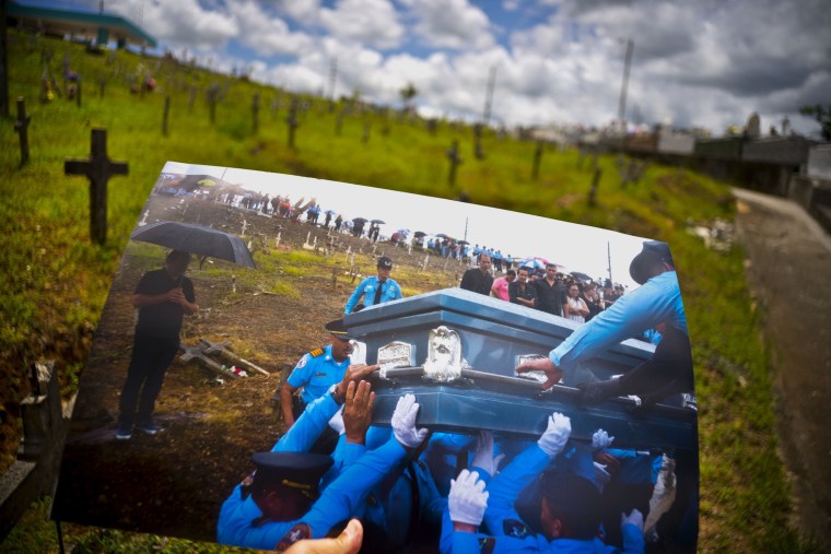 Image: A printed photo taken on Sept. 29, 2017 showing police lifting the coffin of officer Luis Angel Gonzalez Lorenzo, who was killed during the passage of Hurricane Maria when he tried to cross a river in his car, is shown at the same cemetery.