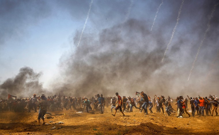 Image: Palestinian protesters take cover from tear gas during a demonstration along the border with Israel