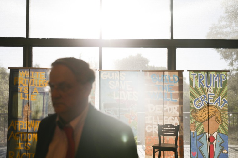 Image: A man walks by banners before a Candace Owens and Charlie Kirk event