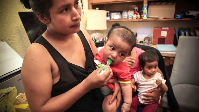 Image: Micaela, 20, holds her 6-month-old infant in her arms as she waits for a volunteer pediatrician to examine him.