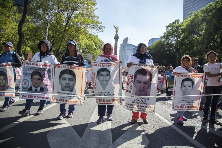 Image: Women march holding banners that show some of the faces of 43 students who went missing nearly four years ago