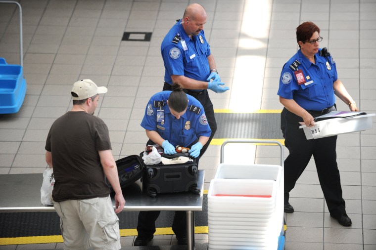 Image: A Transportation Security Administration (TSA) agent checks the luggage of a passenger