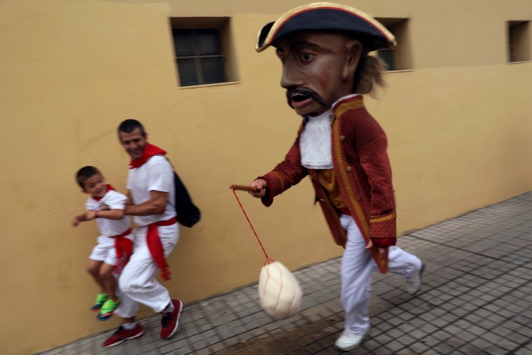 Image: Revellers dodge a \"Kiliki\" ready to hit with his sponge during San Fermin festival's \"Comparsa de gigantes y cabezudos\" (Parade of the Giants and Big Heads) in Pamplona