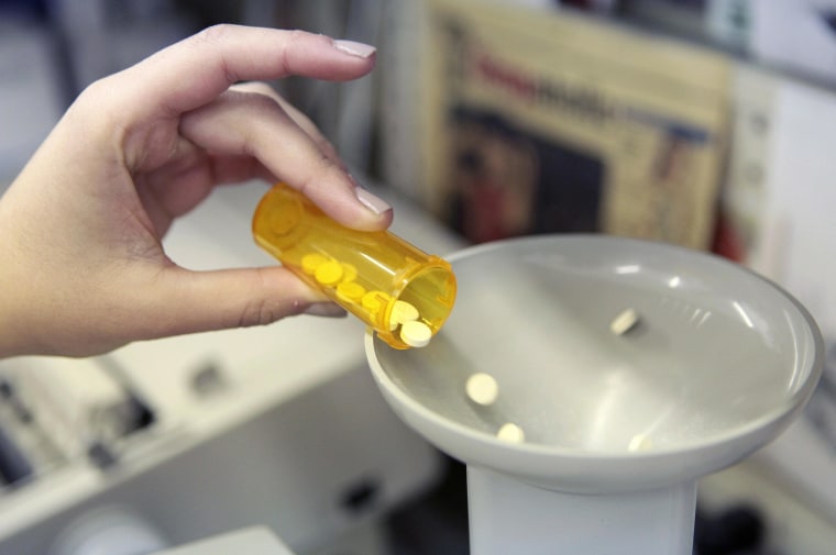 Image: A pharmacy employee dumps pills into a pill counting machine as she fills a prescription.