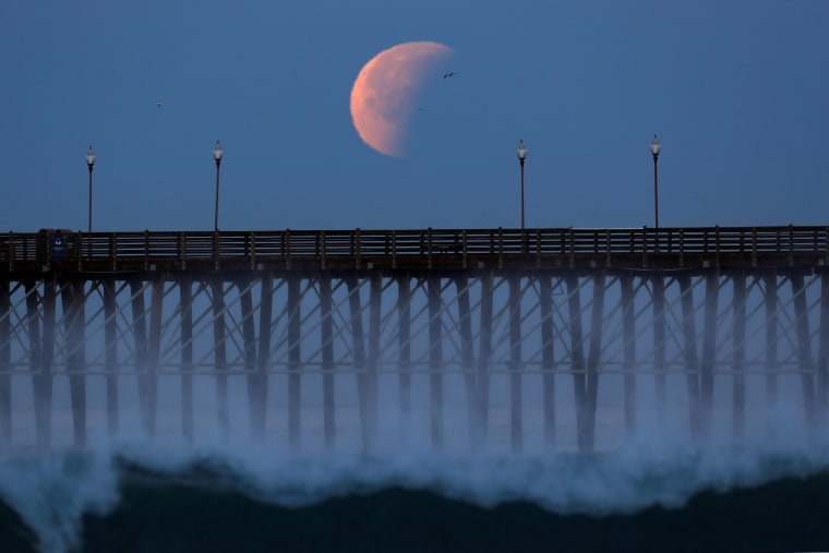 Image: A Blue Moon comes out of a lunar eclipse as it sets past an ocean pier in Oceanside, California