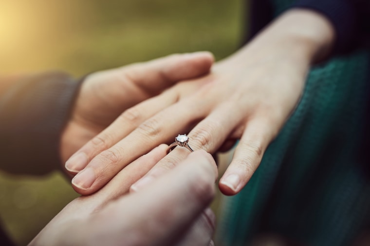 Image: Man putting an engagement ring onto his fiancee's finger outdoors