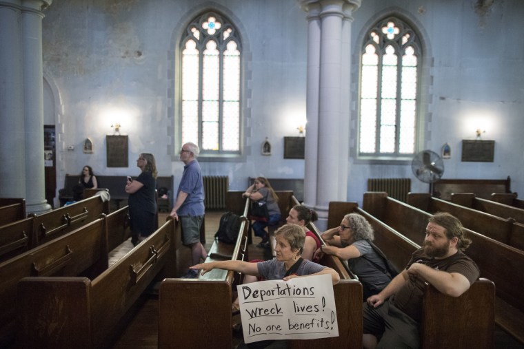 Image: New Sanctuary Coalition volunteer Alice Strum Sutter, center, holds a sign as she watches a news conference