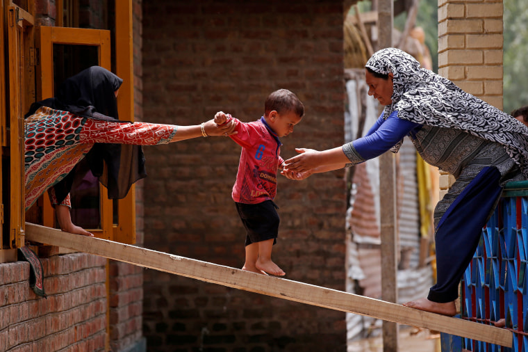 Image: Women help a child to cross over to the other house on a wooden plank after flash floods in Tailbal, on the outskirts of Srinagar
