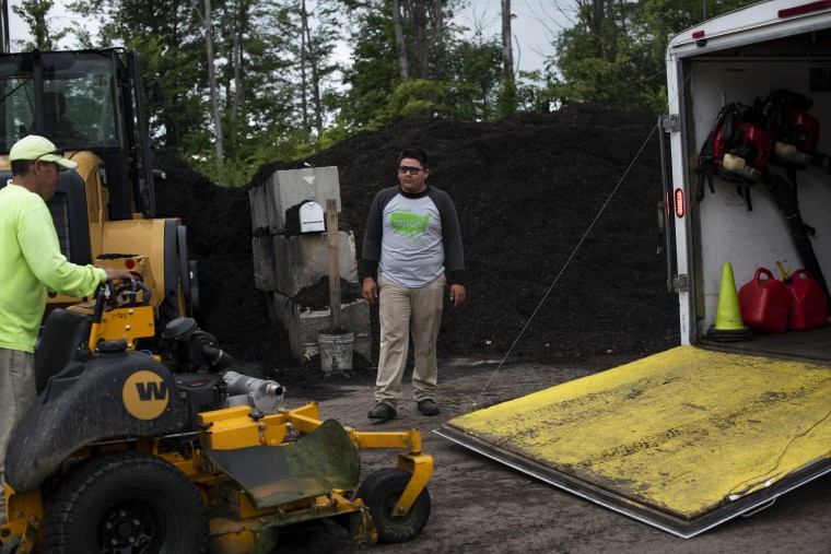 Image: Raul León loads a lawnmower onto a truck with Miguel León Dominguez