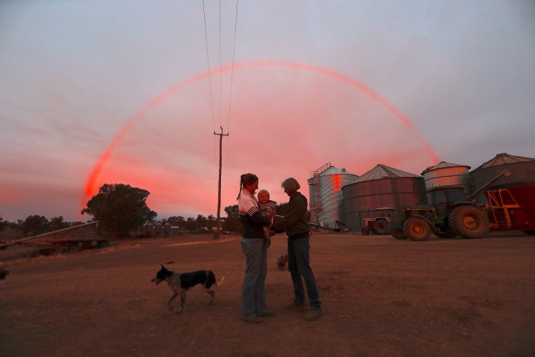 Image: Farmer Tom Wollaston's wife Margo talks with her daughter Natasha and her granddaughter Abbey as a rainbow forms above them at sunset on their drought-effected property, located west of the town of Tamworth