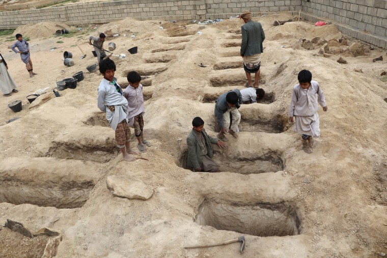 Image: Boys inspect graves prepared for victims of an air strike in the Saada province