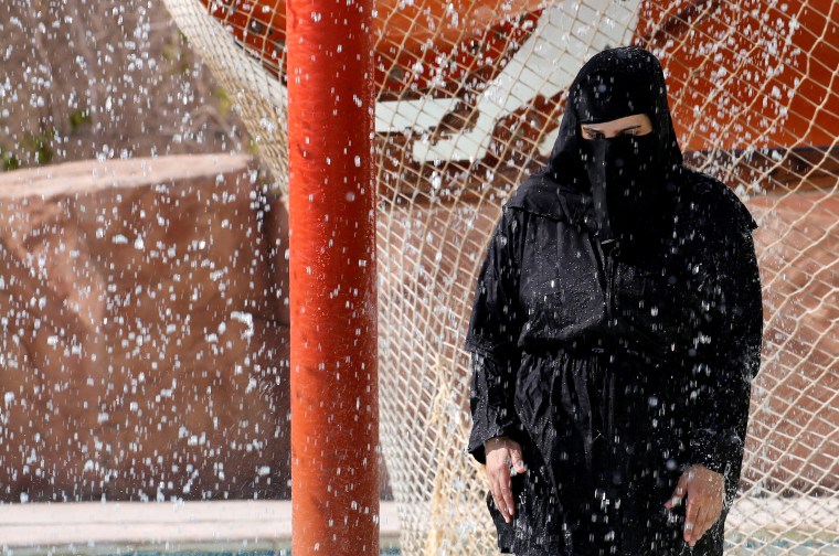 Image: A woman wearing a full veil (niqab) uses a shower to cool off in hot and humid weather inside an Aqua arena during summer holidays at El Ain El Sokhna in Suez, east of Cairo