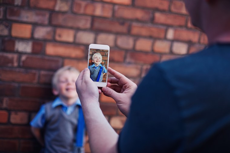 Image: A father uses his cell phone to take a photo of his son on his first day school.