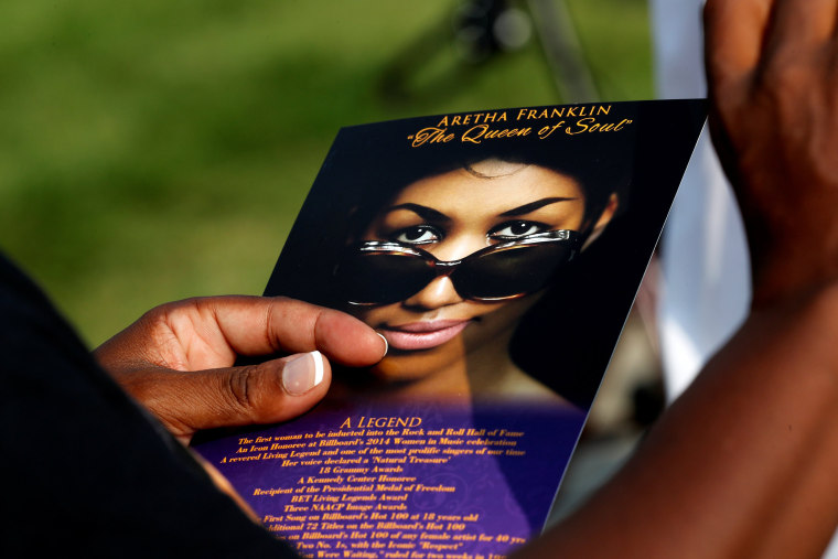 Image: A woman carries a card with an image of Aretha Franklin into the Charles H. Wright Museum of African American History