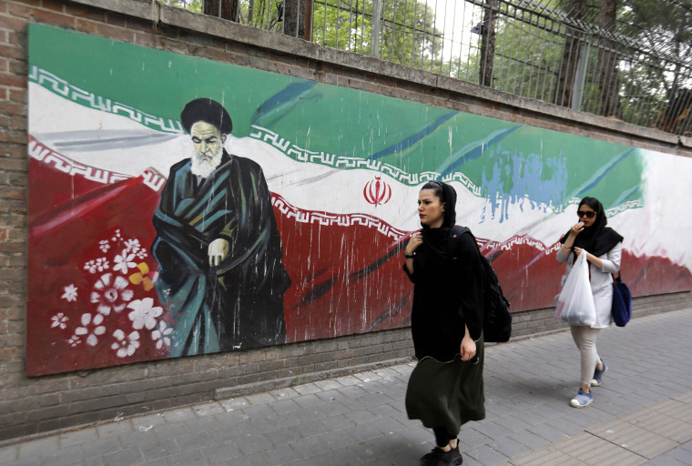 Image: An Iranian woman walks past a mural in Tehran