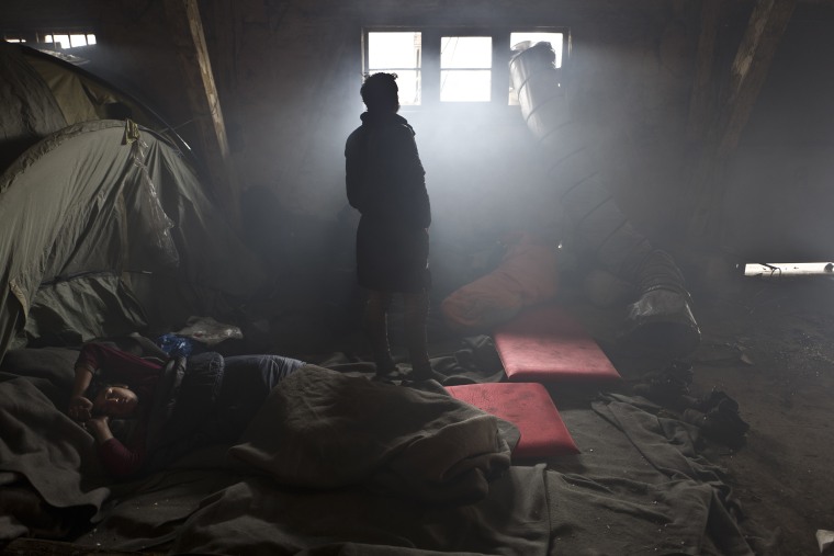 An Afghan refugee sleeps on the ground while another looks out a window in an abandoned warehouse where they and other migrants took refuge in Belgrade, Serbia, on Feb. 1, 2017.