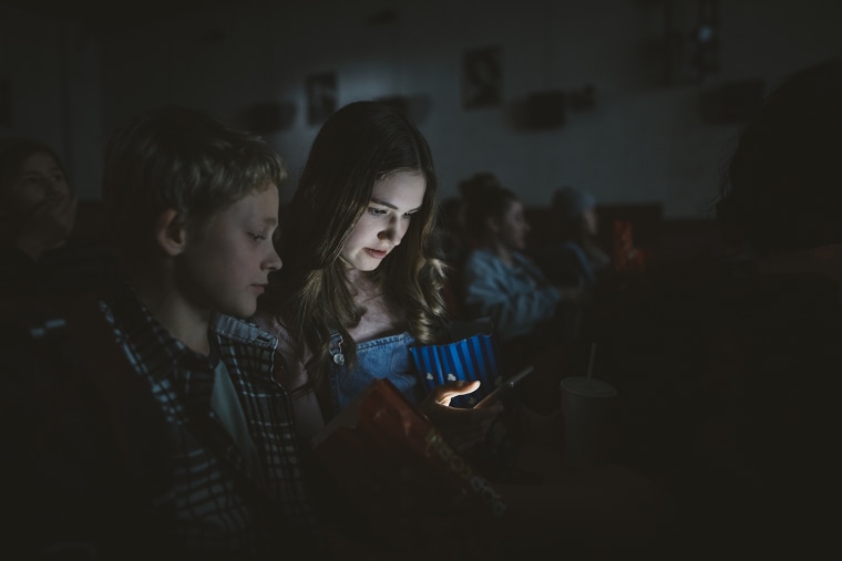 Image: Teen girl texting with smart phone in dark movie theater