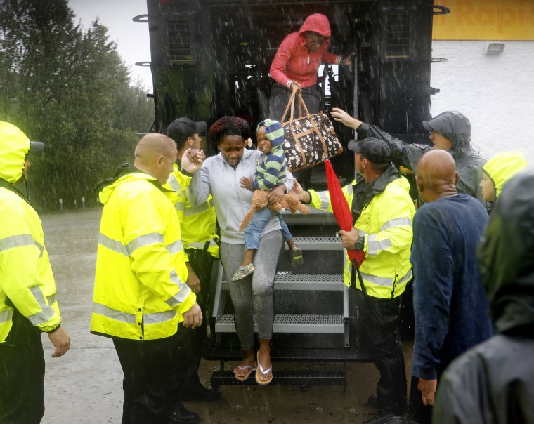 Image: Residents step out of a high water vehicle after being evacuated by the police when their neighborhood began to flood