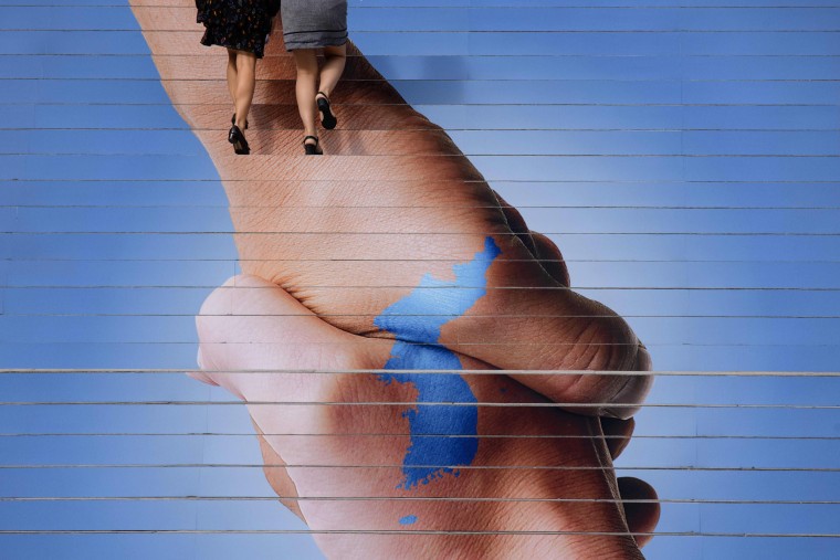 Image: Two women walk up a flight of stairs with an image of a unified Korea