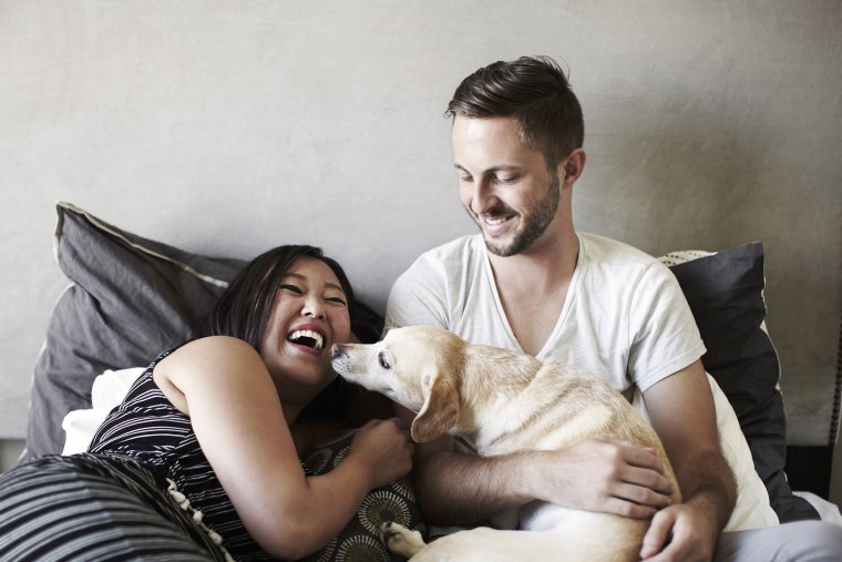 Image: Couple reclining on bed playing with dog