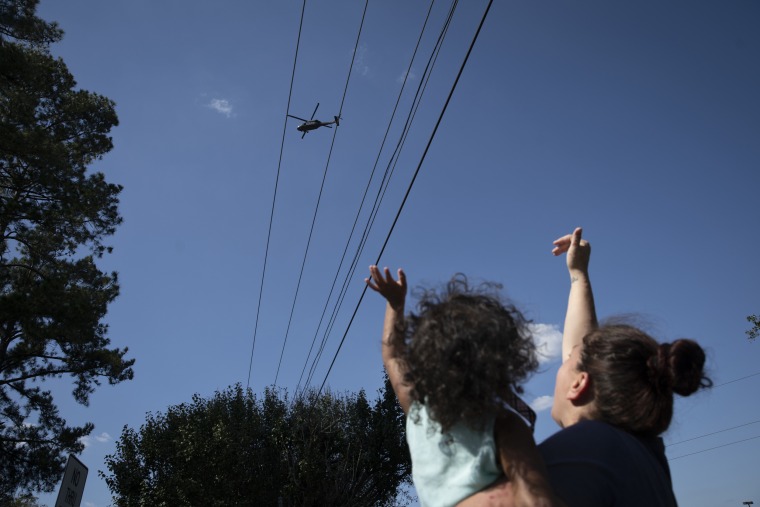 Image: Gloria Orozco-Freeman and her daughter Isobella wave to an approaching helicopter in front of their home in Lumberton
