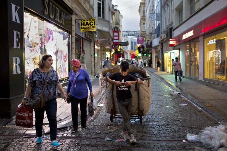 Image: A young man collecting trash looks at his phone near Istanbul's Spice Bazaar.