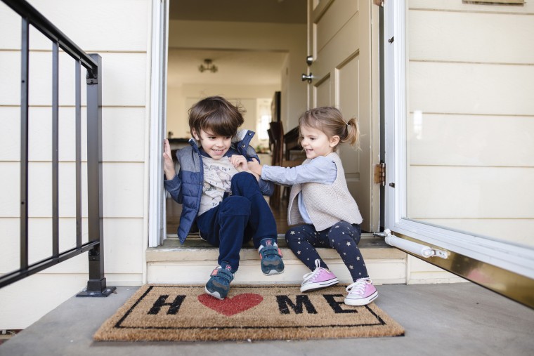 Image: Young boy and girl sitting side by side on the front step of a house, teasing each other and smiling.