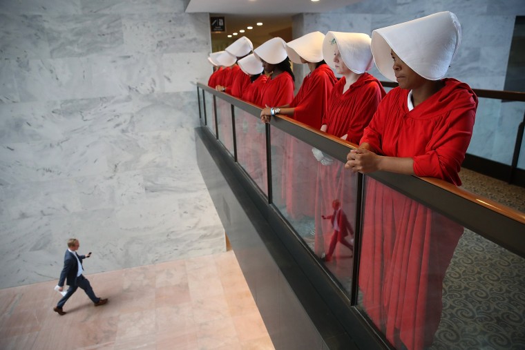 Image:  Protesters dressed in The Handmaid's Tale costumes protest outside the hearing room