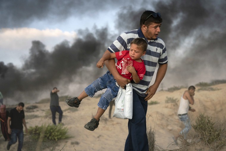 Image: A Palestinian protester carries a boy as he runs from tear gas in Beit Lahiya, northern Gaza Strip.