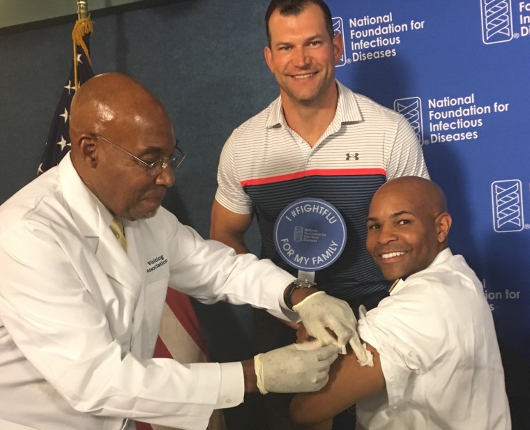 Surgeon General Jerome Adams receives a flu shot as former Cleveland Browns offensive tackle Joe Thomas looks on.