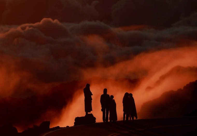 Light illuminates clouds as people watch the sunrise at Haleakea National Park in Hawaii