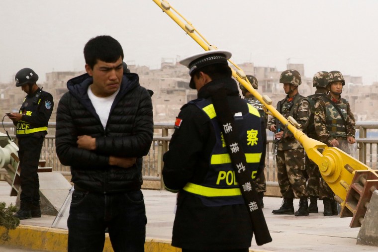 Image: A police officer checks the identity card of a man as security forces keep watch in a street in Kashgar
