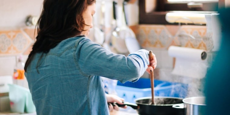 Side View Of Woman Cooking Food In Kitchen At Home