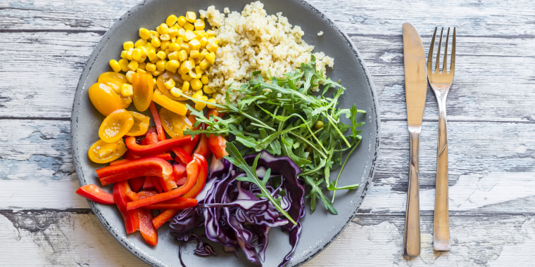 Glass of rainbow salad with bulgur, rocket and different vegetables and bowls with ingredients