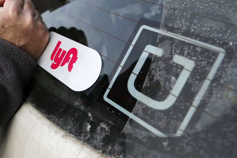 Image: A Lyft logo is installed on a Lyft driver's car next to an Uber sticker in Pittsburgh