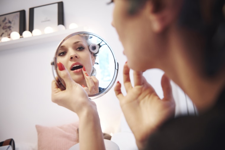 Image: Mirror image of woman applying lipstick