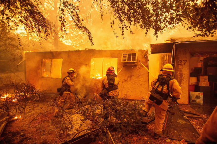 Image: Firefighters push down a wall while battling against a burning apartment complex in Paradise