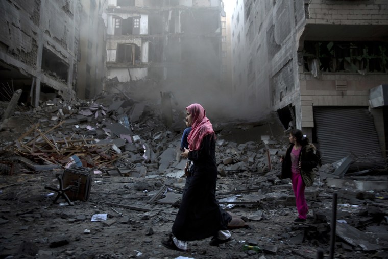 Image: A Palestinian family walks next to a destroyed residential building hit by Israeli airstrikes in Gaza City
