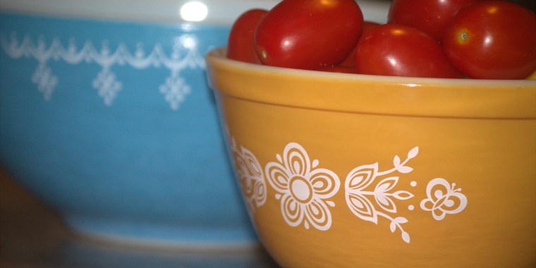 Two vintage Pyrex bowls, one blue and one orange. The orange contains bright red grape tomatoes.