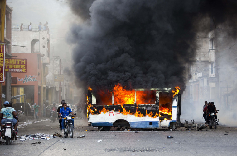 Image: Motorcyclists pass a burning bus set on fire by protesters in Port-au-Prince