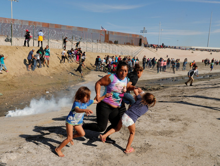 Image: A migrant family, part of a caravan of thousands traveling from Central America en route to the United States, run away from tear gas in front of the border wall between the U.S and Mexico in Tijuana
