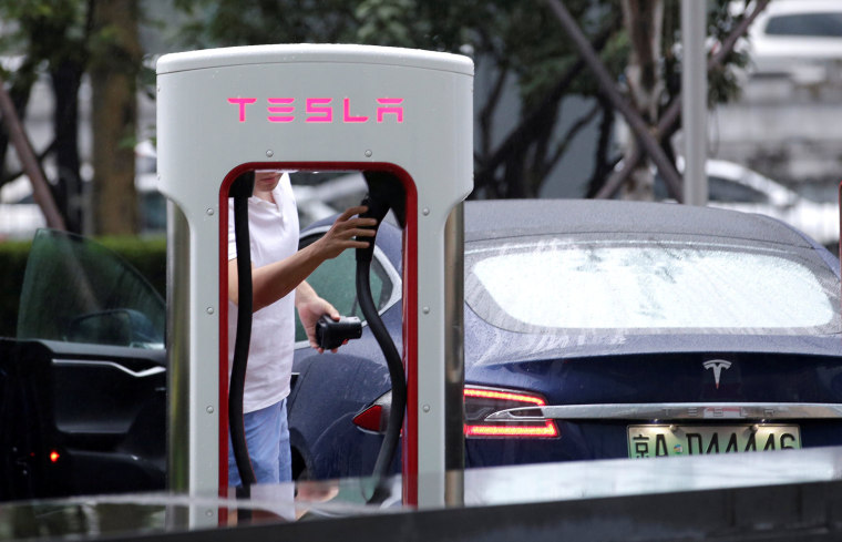 Image: A man charges his Tesla car at  a charging point outside Tesla China headquarters in Beijing