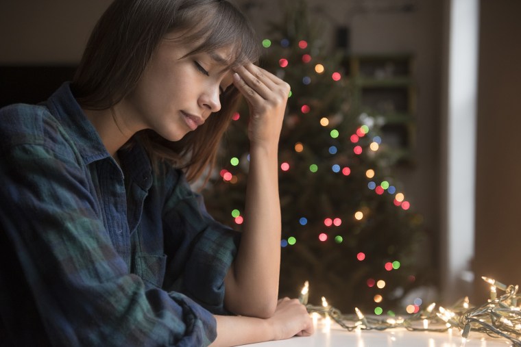Image: Mixed Race woman with headache near Christmas tree